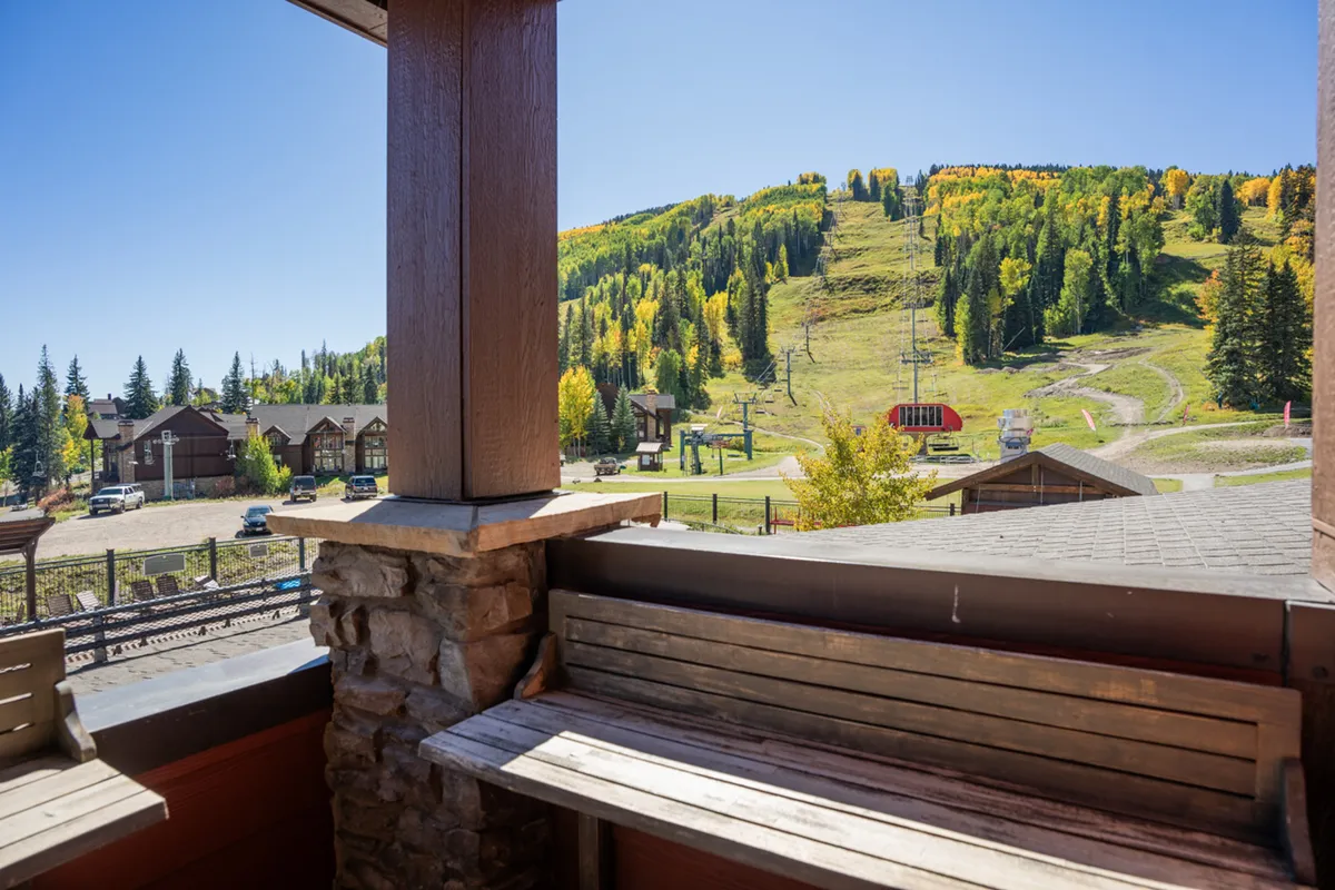 A wide view of the mountain landscape, ski lifts, and autumn foliage, seen from a porch with a wooden bench. The scene captures both the proximity to ski action and the serene beauty of the San Juan Mountains.