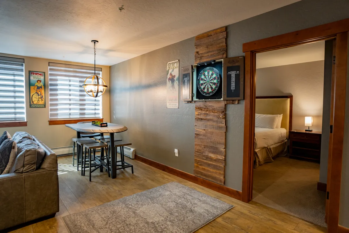 A playful interior space featuring a dartboard, dining table, sofa, and vibrant art posters. The setting is casual and welcoming, ideal for game nights, socializing, and relaxing after a day on the slopes.