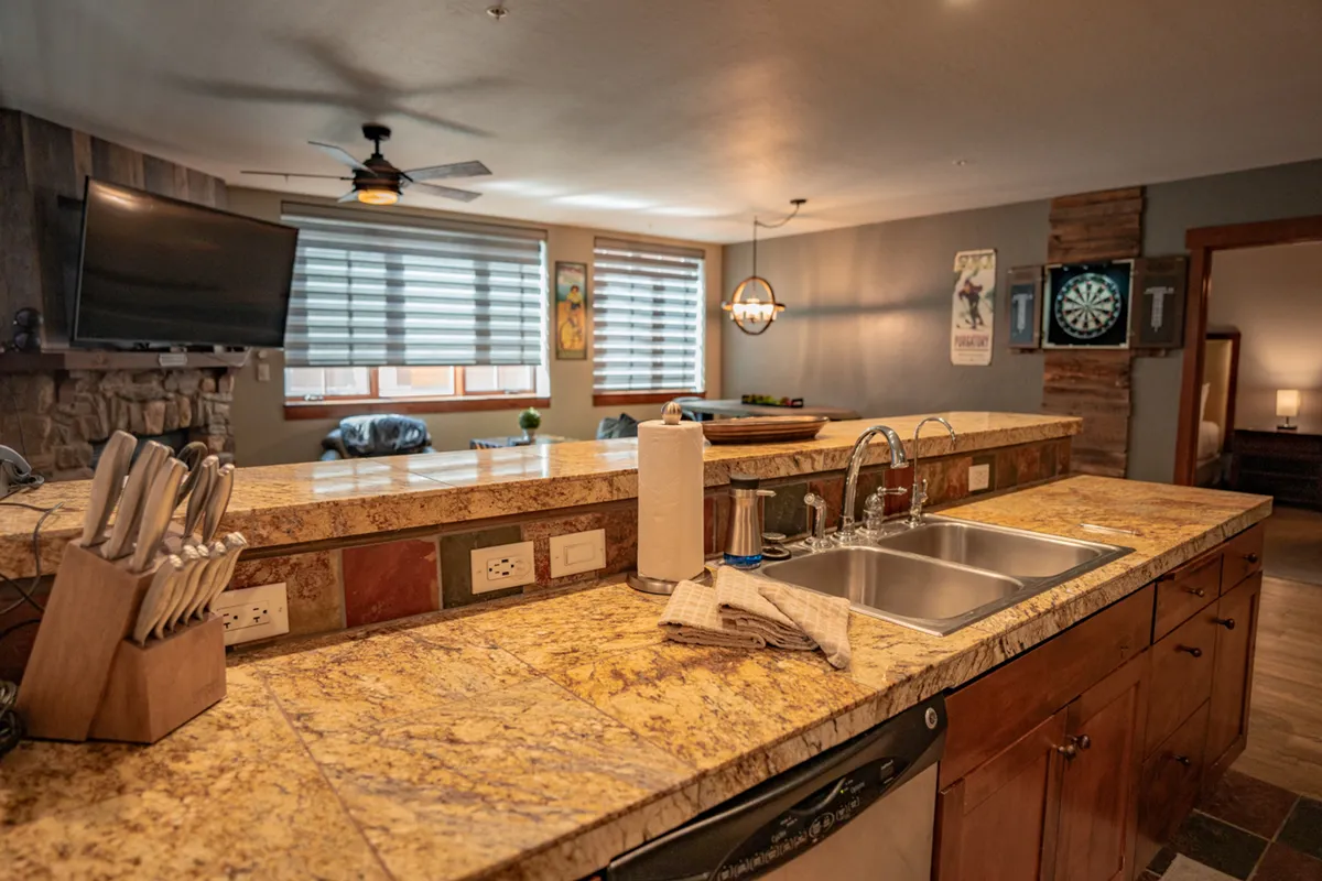 A view of the kitchen’s granite countertop, adjacent dining area, and game area with a dartboard. The image conveys a warm, multifunctional space ideal for both cooking and entertaining.