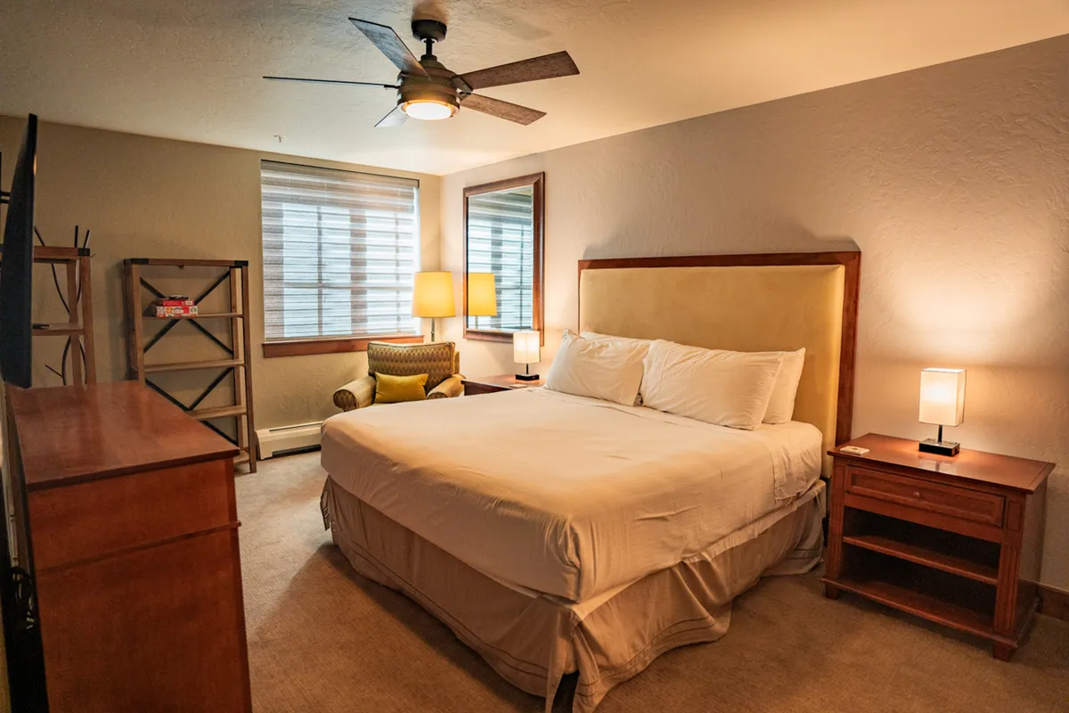 A welcoming bedroom featuring a plush bed flanked by nightstands and lamps, with an inviting armchair and dresser. Soft blankets and natural light make the space ideal for relaxation and restful sleep.