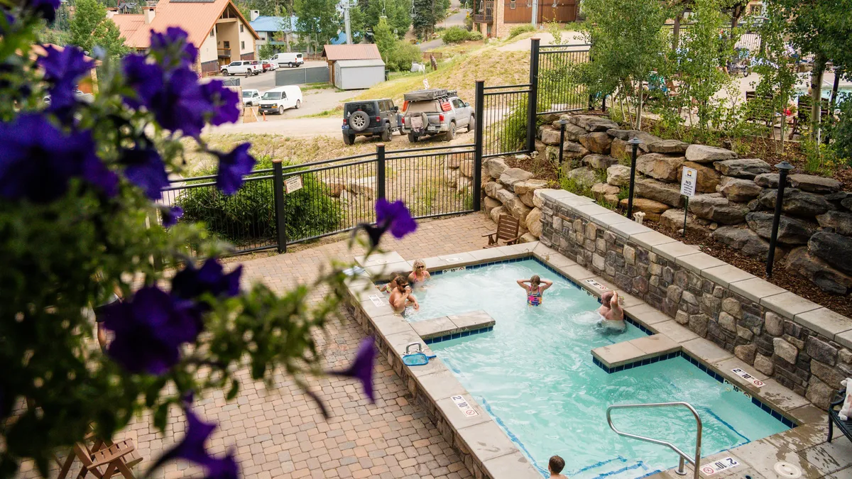 An inviting exterior shot featuring a hot tub and swimming pool surrounded by lush greenery and comfortable seating areas. The scene suggests relaxation, socializing, and the enjoyment of resort wellness amenities in a tranquil outdoor setting.