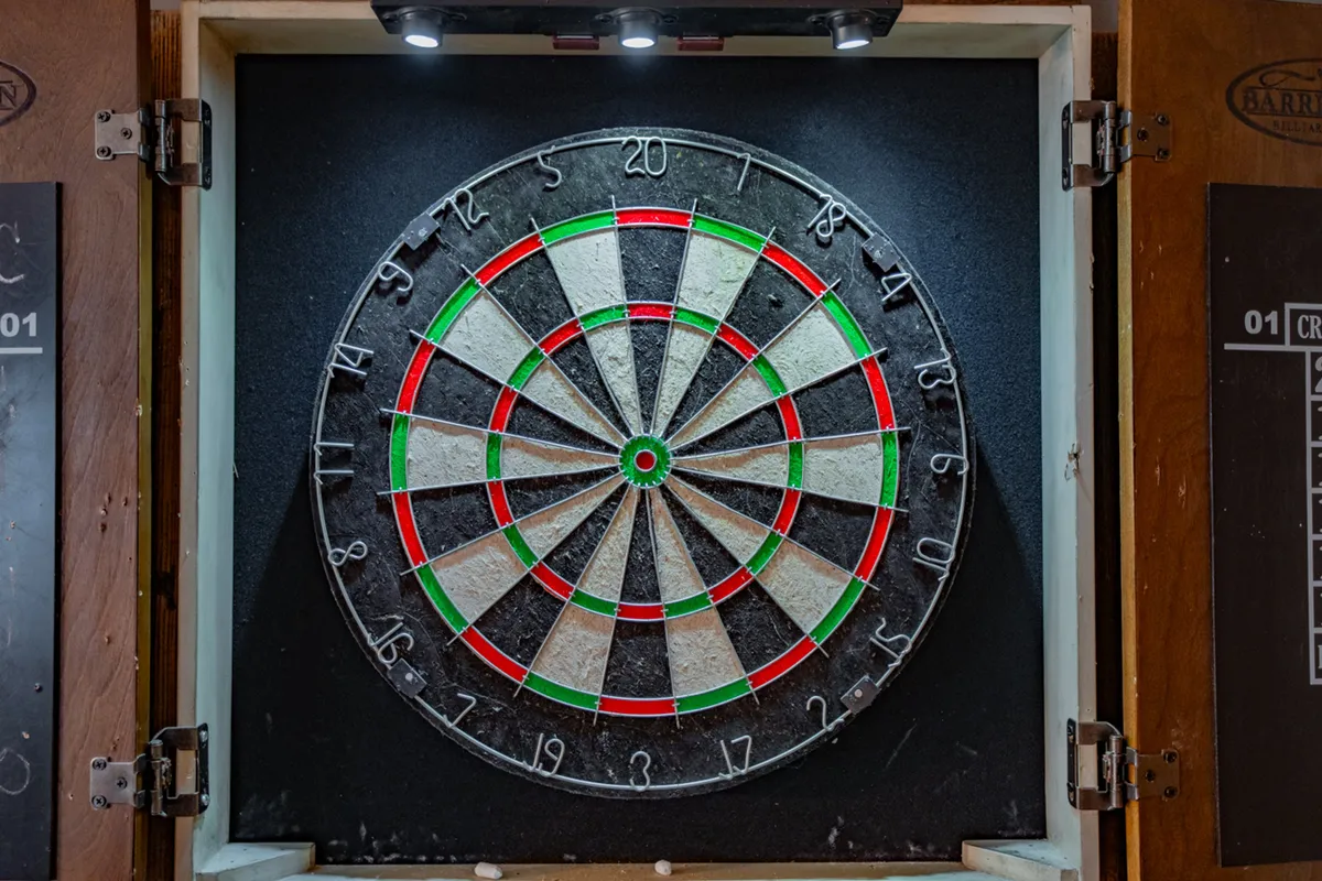 This image features a dartboard surrounded by a cabinet and illuminated by overhead lighting fixtures. The setting suggests a fun, interactive space ideal for informal social gatherings and friendly competitions, likely reflecting the vibe of the family game room described in the section.