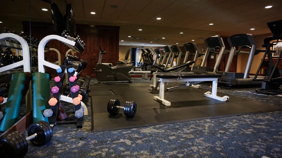 This image features a well-equipped fitness room with dumbbells, treadmills, benches, and other exercise machines. The space is designed for both weightlifting and cardio workouts, with motivational accents and plenty of natural light, hinting at an active lifestyle guests can enjoy while staying at the property.