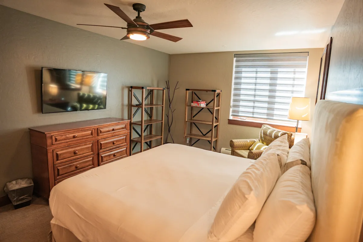 A tranquil bedroom with a plush bed, an inviting armchair, bookshelves, and soft lighting that highlights the peacefulness of the space. The ambiance is intimate and relaxing, designed for unwinding and enjoying quiet moments as a couple.